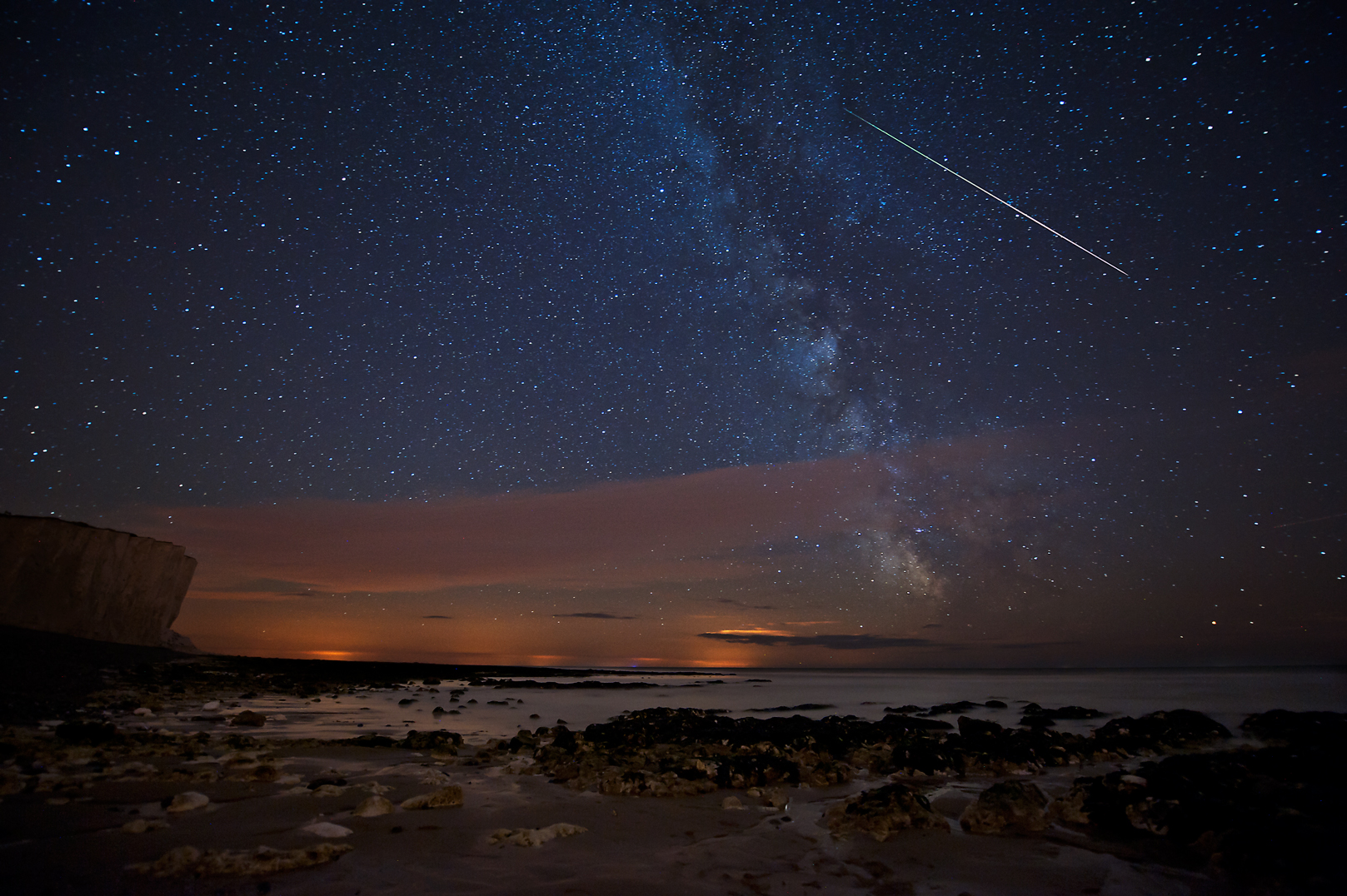 A starry sky with orange glow on the horizon over the sea