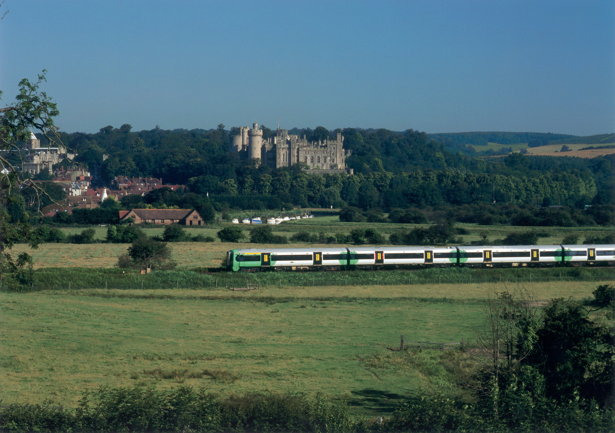 A train goes past a green field with a castle in the distance