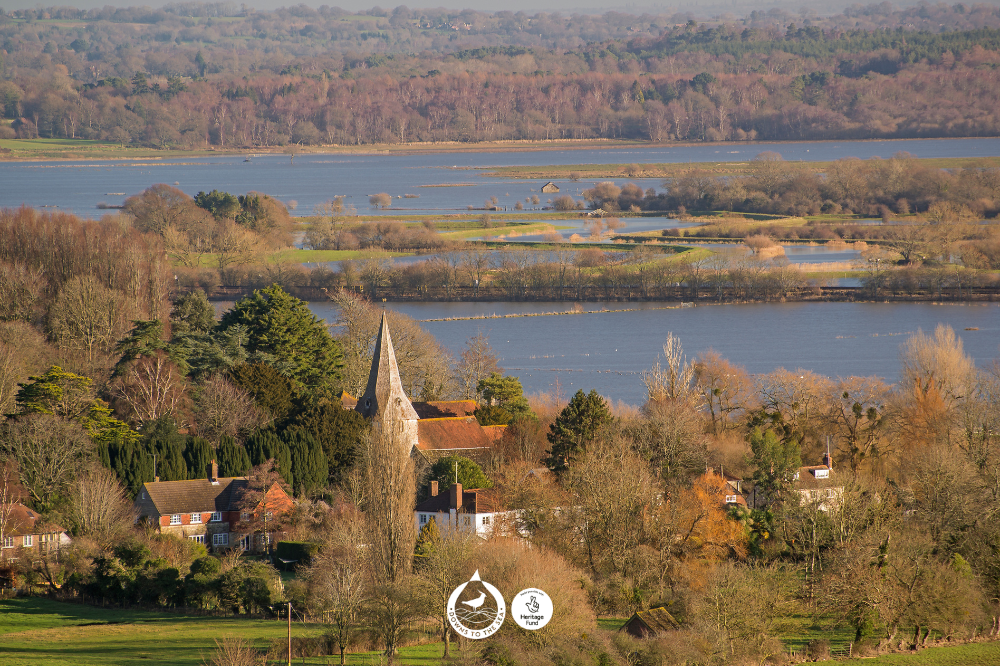 A wetland landscape of ponds and floodplains with a small settlement containing houses and a church with a steeple.
