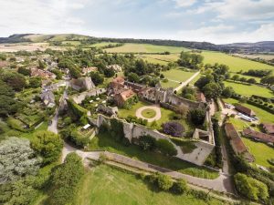 A birdeye view over Amberley village featuring a castle, thatched cottages, rolling green hills and lines of trees