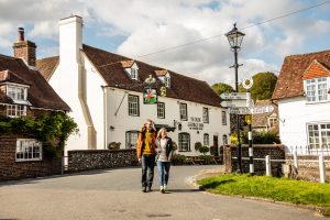 A young couple walking through East Meon village in front of the Ye Olde George public house
