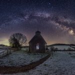 A snow covered church in the middle of a field with the milky way behind it