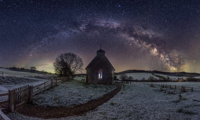 A snow covered church in the middle of a field with the milky way behind it