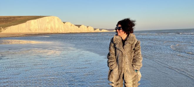 A woman stands on a beach with the white cliffs of Seven Sisters behind her.