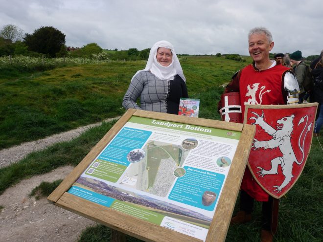 Man and woman in period outfits next to interpretation panel for the Battle of Lewes Walking Trail