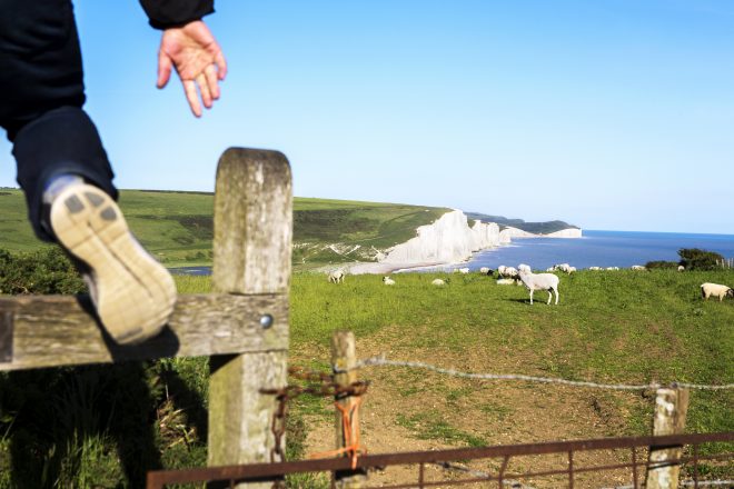 Walker stepping over a stile at Seaford with the Seven Sisters cliffs in the background